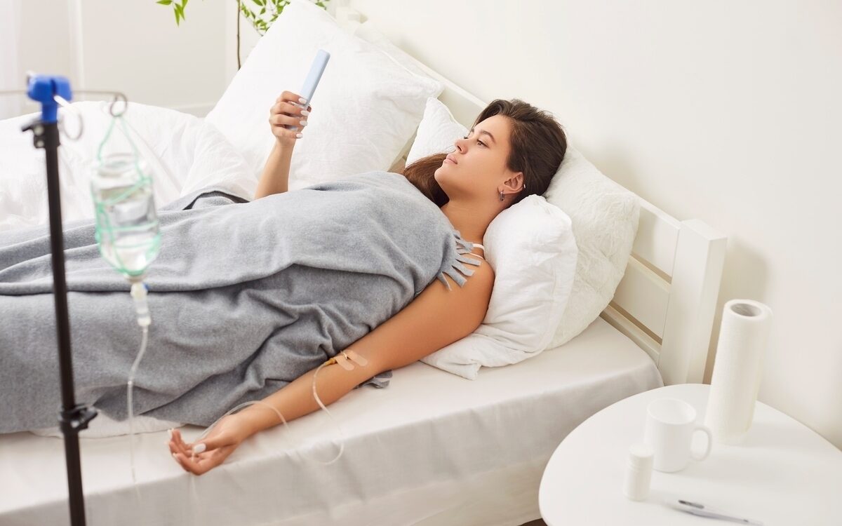 Woman resting in bed receiving IV therapy for illness with drip stand visible at home