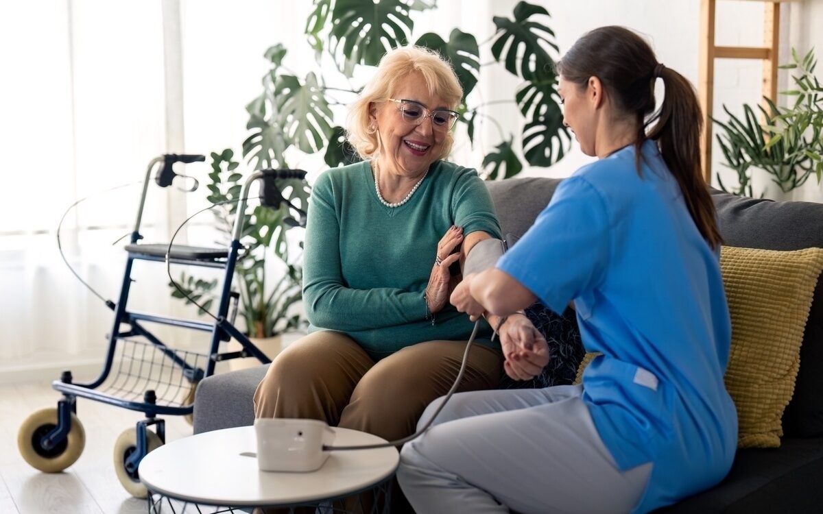 Nurse taking blood pressure of elderly patient during in-home nursing care visit in a warm home setting