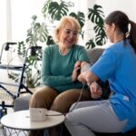 Nurse taking blood pressure of elderly patient during in-home nursing care visit in a warm home setting