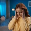 Woman experiencing migraine pain in a dimly lit home setting before IV therapy for migraines