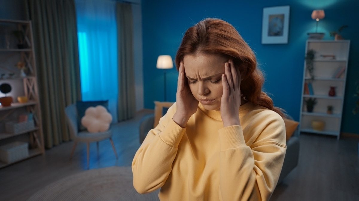 Woman experiencing migraine pain in a dimly lit home setting before IV therapy for migraines
